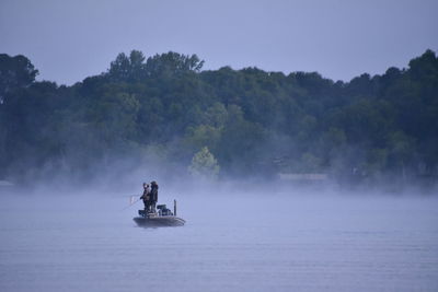 People on boat in lake against trees