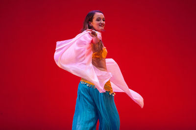Smiling woman belly dancing against red background