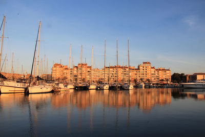 Sailboats moored in harbor by buildings against sky