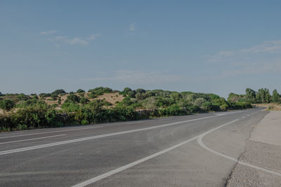 Empty road by trees against sky