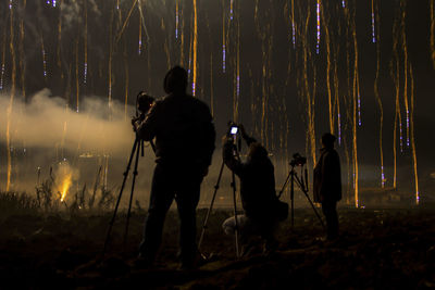 Silhouette man photographing woman with arms outstretched standing at night