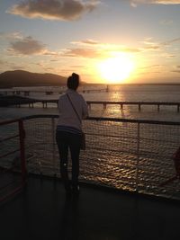 Rear view of silhouette woman standing at beach during sunset