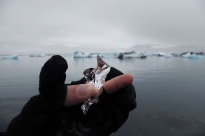 Cropped hand holding wrapper on lake against sky