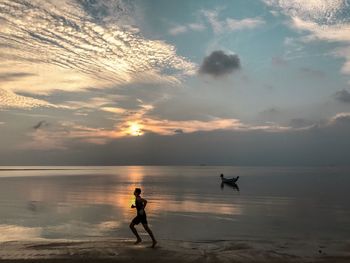 Full length of man running on shore at beach against sky during sunset