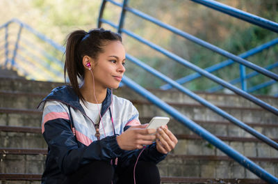 Young woman looking away while listening music through mobile phone