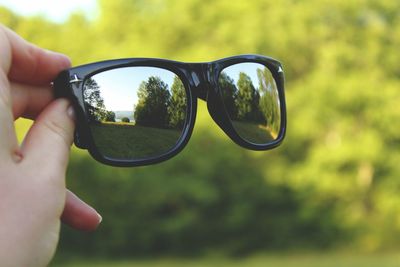 Close-up of hand holding sunglasses against sky