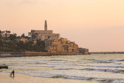 Buildings and st peters church by sea against clear sky during sunset