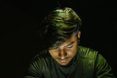 Young man sitting against black background