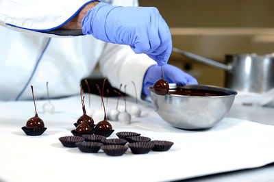 Worker dipping cherries into bowl of chocolate at the chocolate factory

