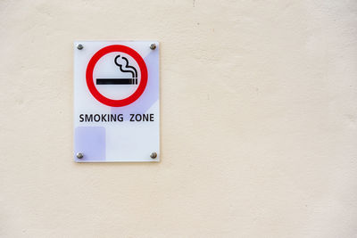 Close-up of smoking zone text on information sign against wall