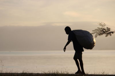 Silhouette man standing on beach against sky during sunset