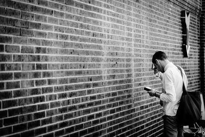 Side view of mature man holding book while standing against brick wall