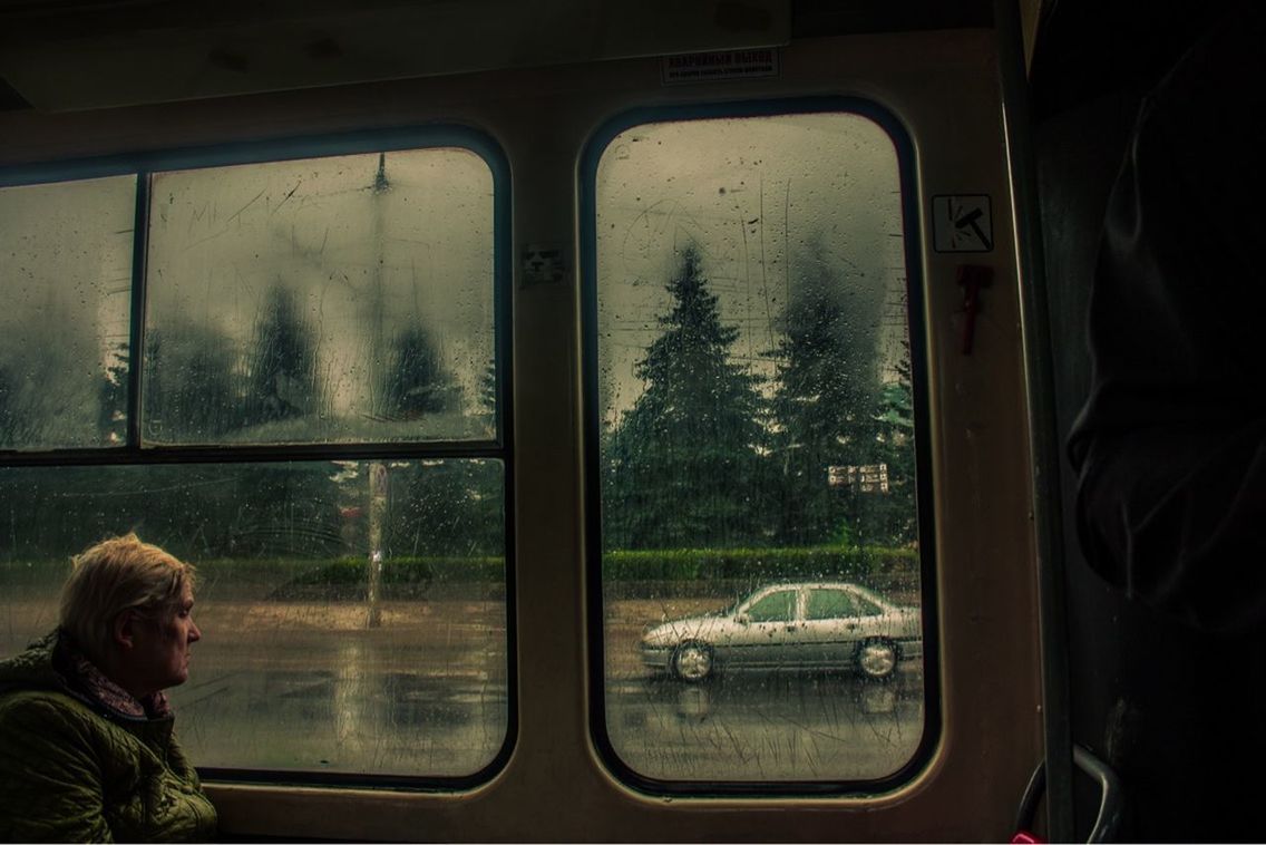 mode of transportation, window, transportation, vehicle interior, train, public transportation, rail transportation, glass - material, train - vehicle, transparent, real people, passenger train, one person, travel, tree, land vehicle, train interior, plant, lifestyles, looking, outdoors