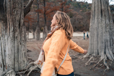 Rear view of woman standing by tree trunk in forest