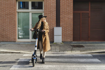 Woman on zebra crossing with electric push scooter against building