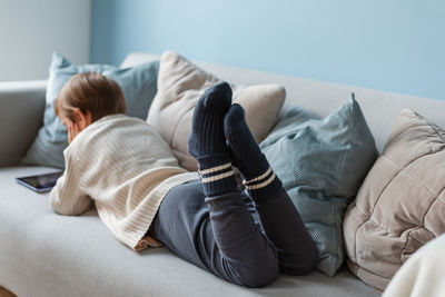 Boy spends time behind a screen on tablet on the sofa in living room. digital device. technologies.