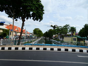 Road by trees against sky in city