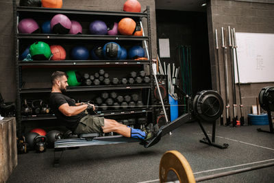 Side view of athletic male with strong body doing exercises on rowing machine in modern sports club