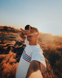 Portrait of young man gesturing while standing on land during sunset