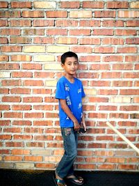 Portrait of teenage boy standing against brick wall
