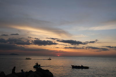 Silhouette people on sea against sky during sunset