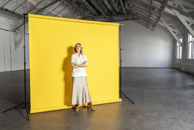 Confident businesswoman with arms crossed standing in front of yellow backdrop