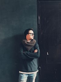 Young man looking away while standing against wall