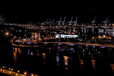 Illuminated city by sea against sky at night