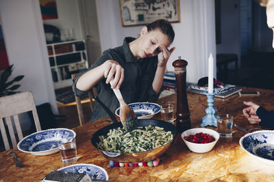 Woman holding wooden spoon in pasta on dining table at home