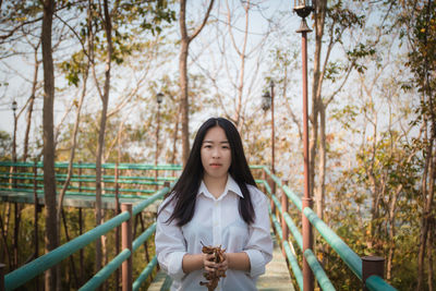 Portrait of young woman standing by railing against trees