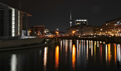 Illuminated buildings by river against sky at night