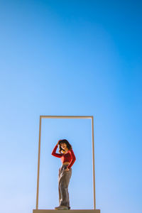 Low angle view of woman standing against clear blue sky