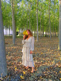 Young woman with leaves amidst trees in forest during autumn