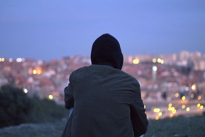 Rear view of man sitting against illuminated city