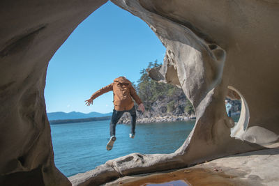 Rear view of person standing on rock by sea against sky