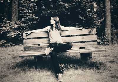 Young woman sitting on bench against trees