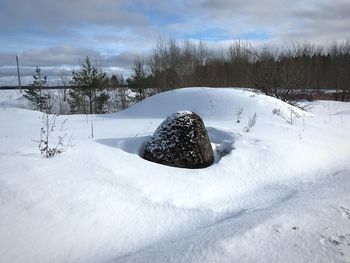 Snow covered field against sky and big stone