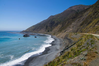 Scenic view of sea and mountains against clear blue sky