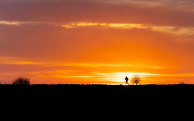 Silhouette people standing on field against orange sky