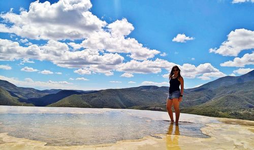 Full length of woman standing in lake on mountain against cloudy sky