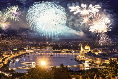 Firework display over illuminated city against sky at night