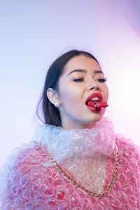 Young woman wearing bubble wrap with toy car in mouth against colored background