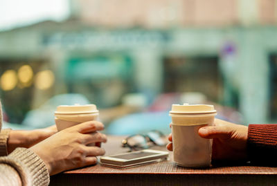 Close-up of hands holding disposable cups at cafe