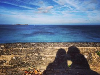 Shadow of people sitting on beach against sky