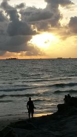 Silhouette man standing on beach against sky during sunset