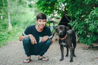 Portrait of smiling young man with dog crouching on field