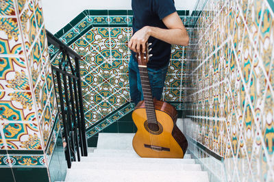 Crop man standing on a staircase with a spanish guitar.
