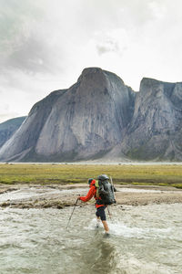 Backpacker crosses river below mountains in akshayak pass