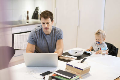 Father using laptop while baby boy sitting at dining table