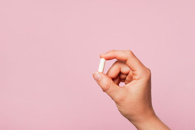 Cropped hand of woman holding pills against pink background